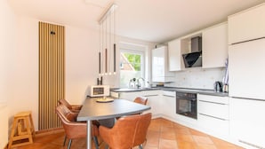 Una cucina moderna con mobili bianchi, un tavolo da pranzo con sedie, un forno a microonde e un forno.