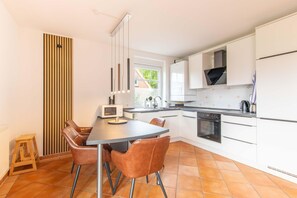 Eine moderne Küche mit weißen Schränken, einem Esstisch mit Stühlen, einer Mikrowelle und einem Backofen.