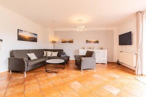 Ein Wohnzimmer mit einer Couch, einem Sessel, einem runden Couchtisch, einem weißen Schrank und einem Flachbildfernseher.