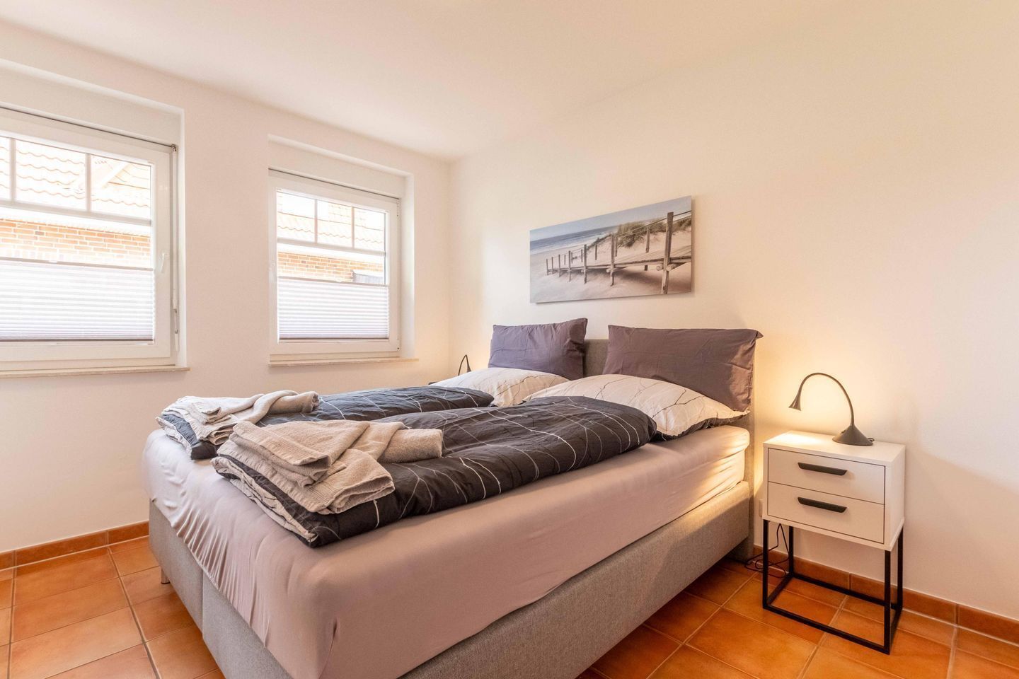 A bedroom with a bed, two windows, a nightstand, and a lamp.