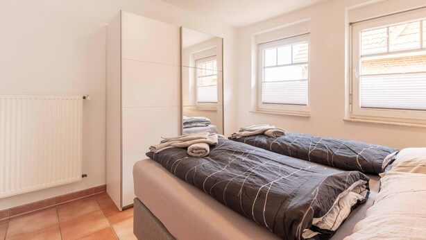 Camera da letto con due letti, termosifone e finestra con persiane.