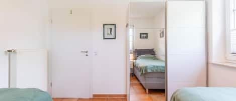 Een slaapkamer met een bed, een kast, een radiator en een deur naar een andere kamer.