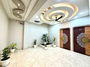 Um hall de entrada com piso de mármore, teto com iluminação embutida, plantas em vasos e portas de madeira com detalhes em metal.