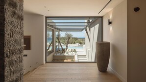 Un interior moderno con una pared de piedra, un jarrón grande y vistas a una piscina y árboles.