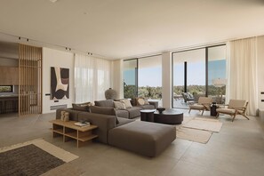 A modern living room with a sofa, ottoman, coffee table, and chairs, large windows with curtains, and a view of the outdoors. - Eleven Sundays Retreat | Beach Escape by etouri (Chania)