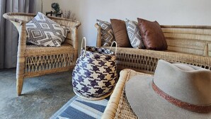 A wicker sofa with patterned cushions, a woven bag, and a hat on a rug.