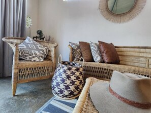 A wicker sofa with patterned cushions, a woven bag, and a hat on a rug.