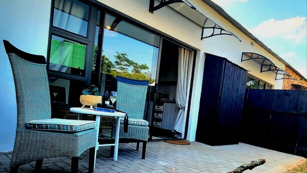 A patio with wicker chairs and a table, a sliding glass door, and a dark fence.