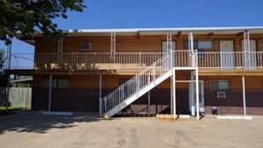Un edificio de dos pisos con una escalera que conduce al nivel superior, un área cercada y un cielo despejado.