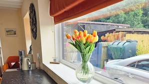 Un plan de travail de cuisine orné d’un vase de tulipes, une fenêtre donnant sur une voiture et sur de la verdure, et un rideau rouge.