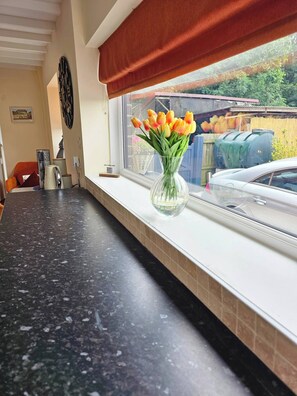 A kitchen counter with a vase of tulips, a window with a view of a car and greenery, and a red curtain. - A romantic retreat in a stunning setting (Nottinghamshire)