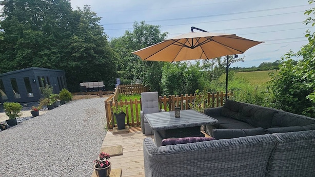 Une terrasse dotée d’un grand canapé en osier, d’un parasol et d’une petite structure en bois.