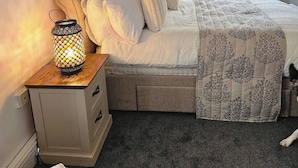 Une chambre à coucher avec un lit, une table de chevet avec une lampe, une fenêtre et un radiateur.