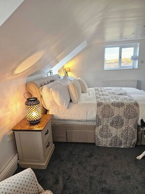 A bedroom with a bed, a nightstand with a lamp, a window, and a radiator. - A romantic retreat in a stunning setting (Nottinghamshire)