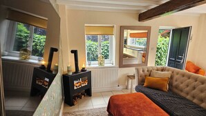 Une pièce chaleureuse avec un canapé, un tapis à motifs, un radiateur et une fenêtre donnant sur un paysage verdoyant.