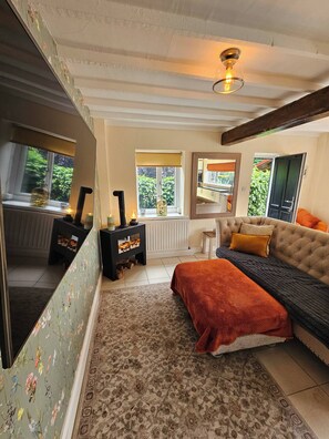 A cozy room with a sofa, a patterned rug, a radiator, and a window with a view of greenery. - A romantic retreat in a stunning setting (Nottinghamshire)