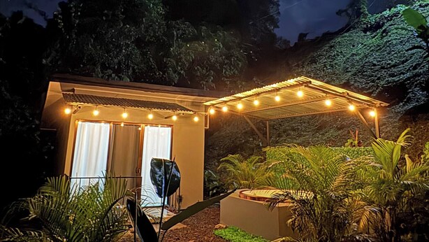 A small house with a covered porch, surrounded by tropical plants and a night sky. - Tranquil Mountain Lodge Retreat in Fortuna, Costa Rica (Zeta trece)