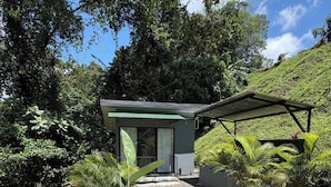 A small, modern structure with a covered patio, surrounded by lush greenery and a gravel path. - Tranquil Mountain Lodge Retreat in Fortuna, Costa Rica (Zeta trece)