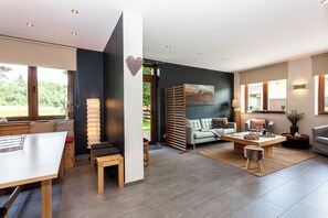 Ein modernes Wohnzimmer mit Essbereich, einer Couch, einem Couchtisch und Blick ins Grüne.
