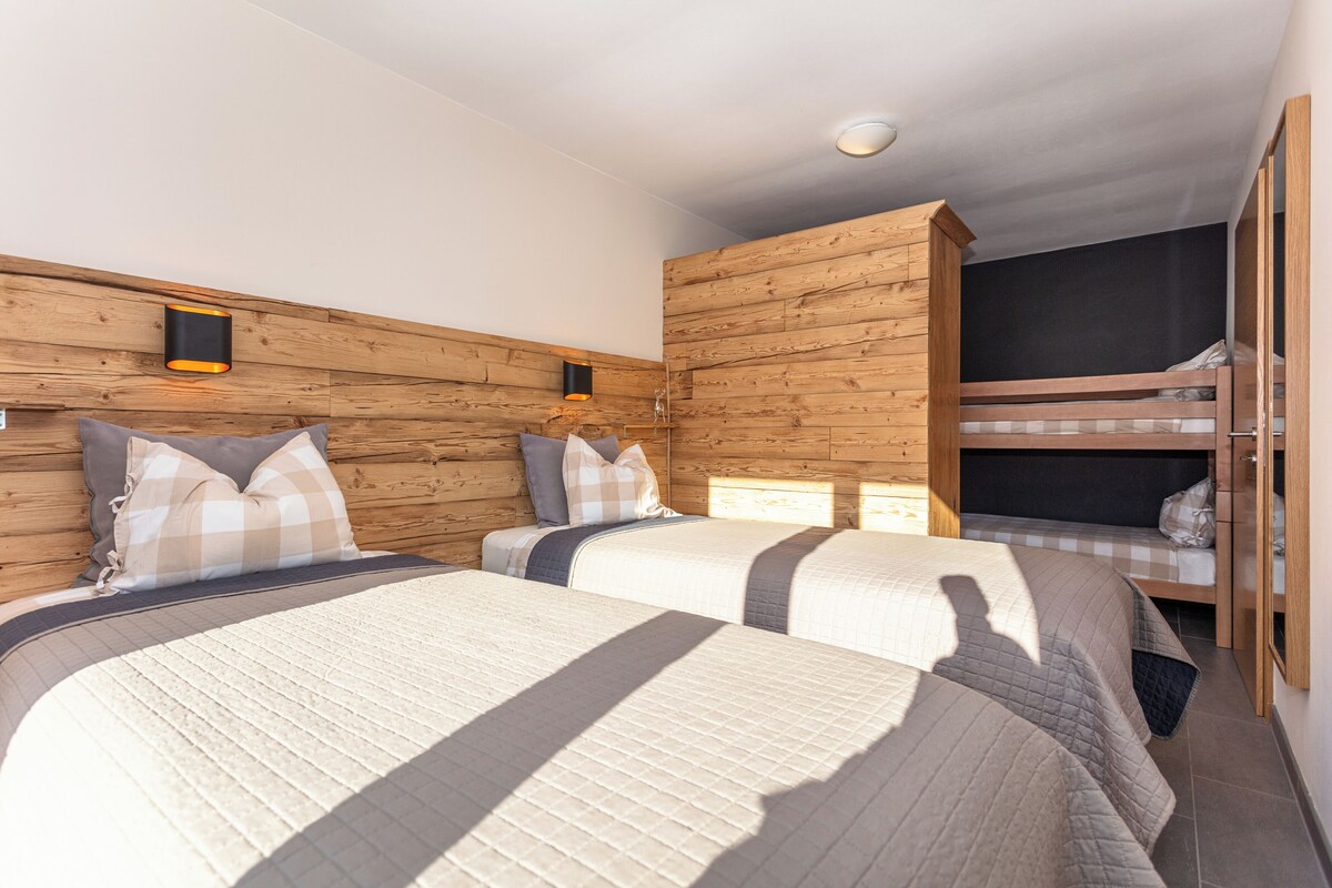 Quarto com duas camas, painéis de madeira e uma beliche.