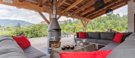A covered outdoor seating area with a wood-burning stove, a sofa, and a view of the surrounding landscape.