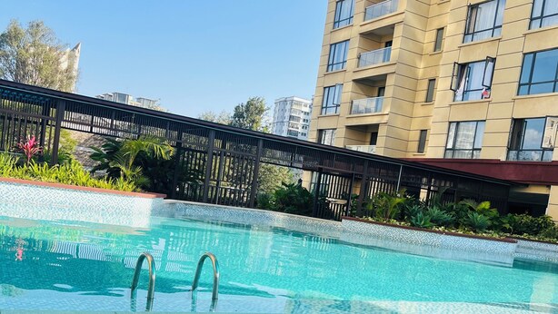 A swimming pool with clear water, a glass of wine on a table, and a building in the background. - Luxury 2-bedroom, Modern Apartment, Elegant, Spacious in Kilimani Nairobi (Nairobi)