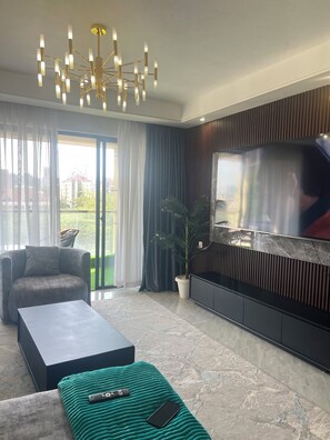 A modern living room with a sofa, a coffee table, a TV mounted on a wall, and a chandelier. - Luxury 2-bedroom, Modern Apartment, Elegant, Spacious in Kilimani Nairobi (Nairobi)
