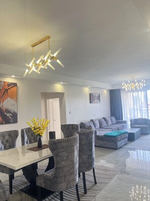A modern living room with a sofa, a dining area with chairs and a table, and a chandelier. - Luxury 2-bedroom, Modern Apartment, Elegant, Spacious in Kilimani Nairobi (Nairobi)