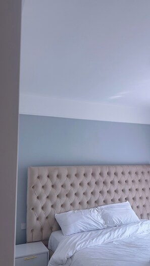 Ein Schlafzimmer mit einem gepolsterten Kopfteil, weißer Bettwäsche und einem Nachttisch mit Schublade.