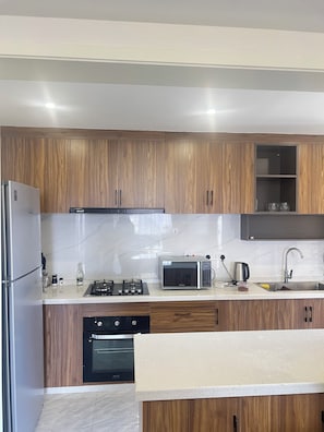 A modern kitchen with wooden cabinets, a stainless steel refrigerator, a microwave, a gas stove, and a dishwasher. - Luxury 2-bedroom, Modern Apartment, Elegant, Spacious in Kilimani Nairobi (Nairobi)