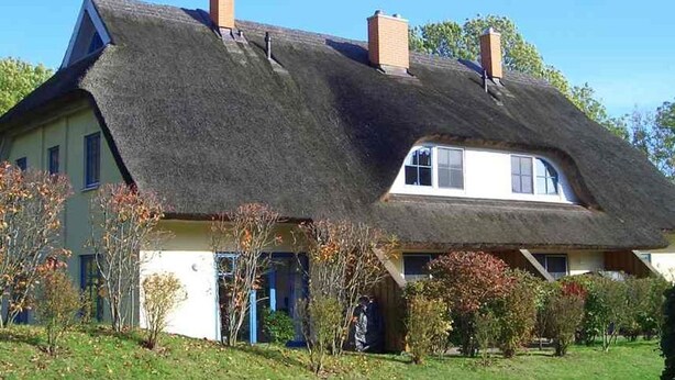 A house with a steeply pitched thatched roof, multiple chimneys, and a well-maintained garden. - Malve 3 Thatched-Roof House - Malve 3 Vacation Home – Thatched-Roof Vacation with a Fireplace and Wallbox (Poseritz)
