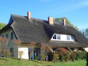 Ein Haus mit einem steilen, strohgedeckten Dach, mehreren Schornsteinen und einem gepflegten Garten.