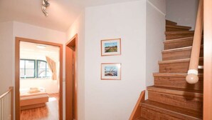 A staircase with wooden steps and a handrail, a hallway with wooden flooring, and two framed pictures on the wall. - Malve 3 Thatched-Roof House - Malve 3 Vacation Home – Thatched-Roof Vacation with a Fireplace and Wallbox (Poseritz)