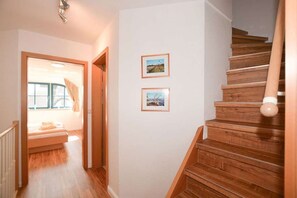A staircase with wooden steps and a handrail, a hallway with wooden flooring, and two framed pictures on the wall. - Malve 3 Thatched-Roof House - Malve 3 Vacation Home – Thatched-Roof Vacation with a Fireplace and Wallbox (Poseritz)