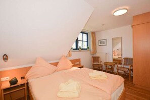 Ein Schlafzimmer mit Bett, Nachttisch, Lampe, Fenster und Blick ins Freie.