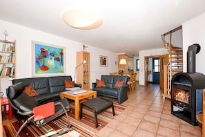 Ein Wohnzimmer mit Sofa, Hocker, Couchtisch, Kamin, Bücherregal und einem Gemälde an der Wand.