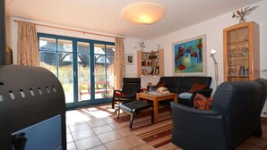 A living room with a sofa, armchair, coffee table, bookshelf, and a painting on the wall. - Malve 3 Thatched-Roof House - Malve 3 Vacation Home – Thatched-Roof Vacation with a Fireplace and Wallbox (Poseritz)