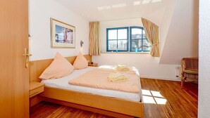 A bedroom with a wooden bed, a nightstand, a chair, a window with curtains, and a framed picture on the wall. - Malve 3 Thatched-Roof House - Malve 3 Vacation Home – Thatched-Roof Vacation with a Fireplace and Wallbox (Poseritz)