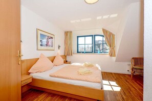 A bedroom with a wooden bed, a nightstand, a chair, a window with curtains, and a framed picture on the wall. - Malve 3 Thatched-Roof House - Malve 3 Vacation Home – Thatched-Roof Vacation with a Fireplace and Wallbox (Poseritz)