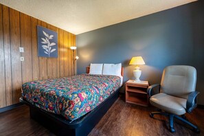 A room with a bed, a chair, a nightstand, and a wall-mounted lamp. - King Bed | Non-Smoking (Portland OR)