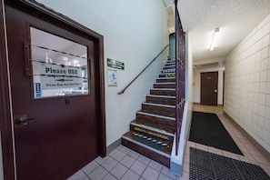A staircase with handrails, a door with a sign instructing to use the night window, and a sign for ice vending machine updates. - King Bed | Non-Smoking (Portland OR)