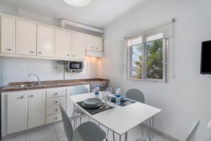 A compact kitchen with white cabinets, a microwave, a gas stove, and a dining table with chairs. - Charming 1-Bedroom Apartment with Ocean View in Arona (Arona)