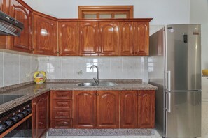 A kitchen with wooden cabinets, a stainless steel refrigerator, and a granite countertop. - Charming Bungalow Rental in Abades, Spain - Perfect Family Retreat (Abades)