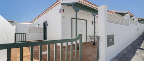 Un edificio blanco con techo de tejas, una verja verde y un patio empedrado.