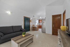 A living room with a sofa, coffee table, TV, and kitchen in the background. - Charming Bungalow Rental in Abades, Spain - Perfect Family Retreat (Abades)