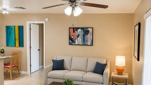 Ein Wohnzimmer mit Deckenventilator, einer Couch, einem Couchtisch, einer Lampe und Kunstwerken an den Wänden.