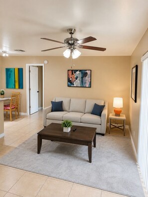 A living room with a ceiling fan, a sofa, a coffee table, a lamp, and artwork on the walls.