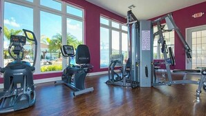 Ein Fitnessstudio mit Cardiogeräten, Krafttrainingsgeräten und großen Fenstern mit Blick auf Palmen.