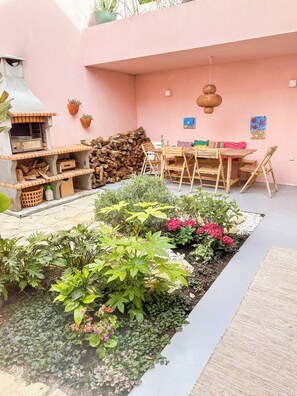 Eine Terrasse mit Holztisch und -stühlen, einem Backofen aus Ziegeln und einem Garten mit verschiedenen Pflanzen und Blumen.
