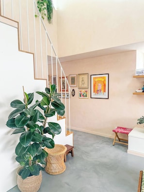 Eine Treppe mit weißer Geländer, ein Blumentopf, ein Korbstuhl und gerahmte Kunstwerke an der Wand.